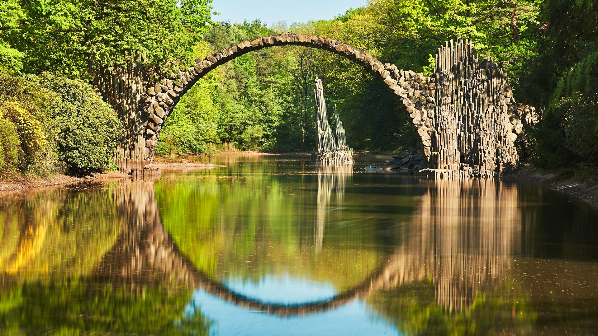 Weak stone bridge over lake in Germany, creating beautiful reflection