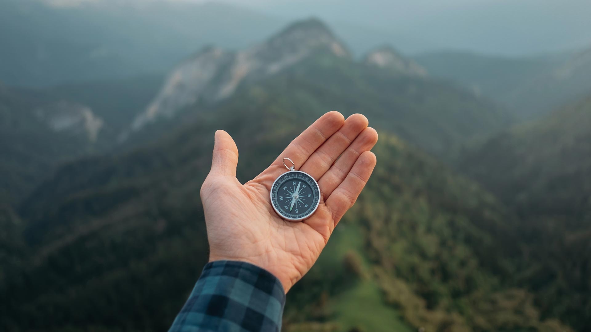 Person holding a compass in their hand whilst on a mountain