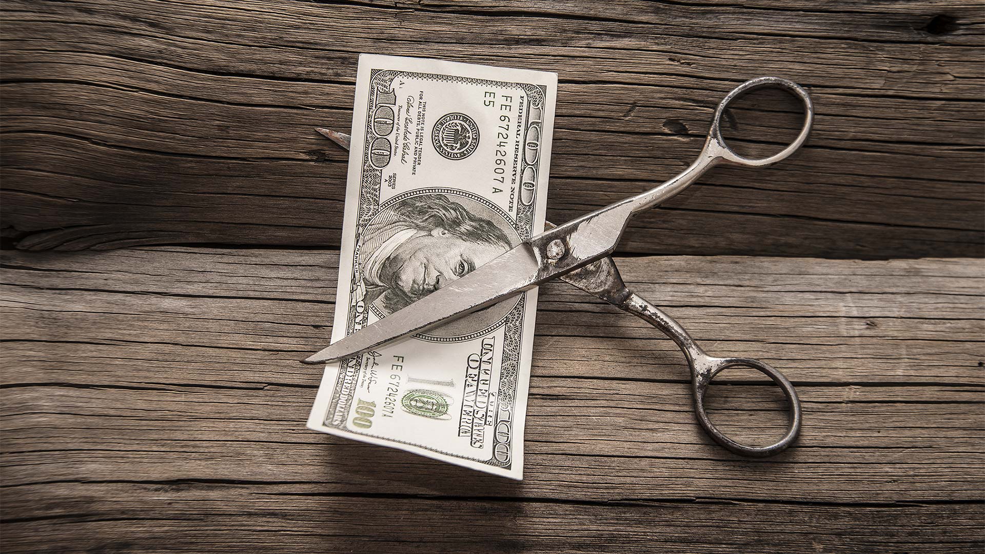 Scissors about to cut in half a one-hundred dollar note