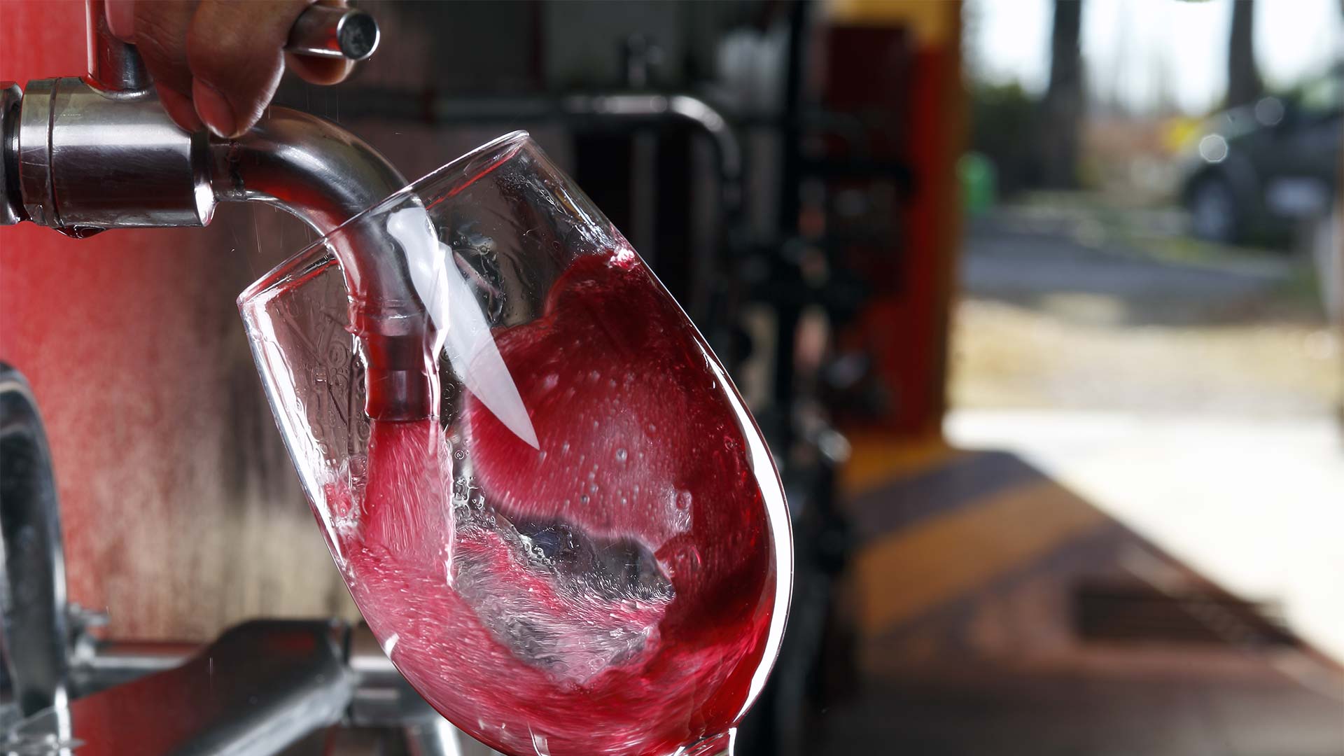 Glass of red wine being poured by tap