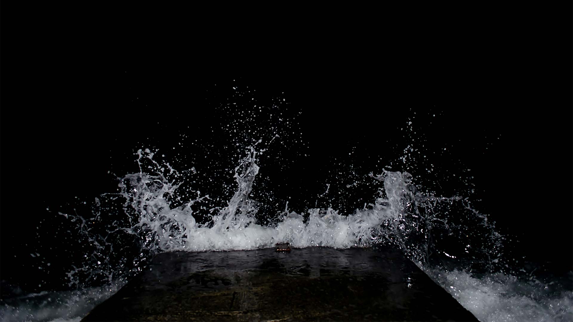 Wave splashing against dark wall at night
