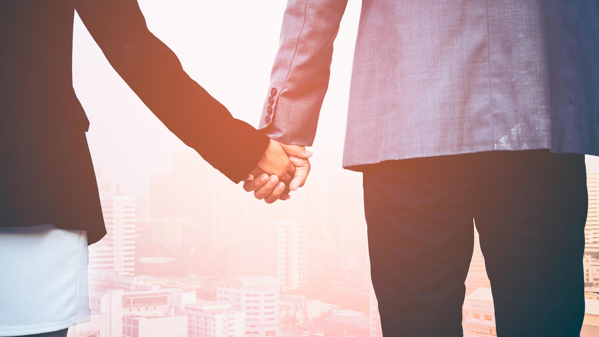 Two business people holding hands in front of the city