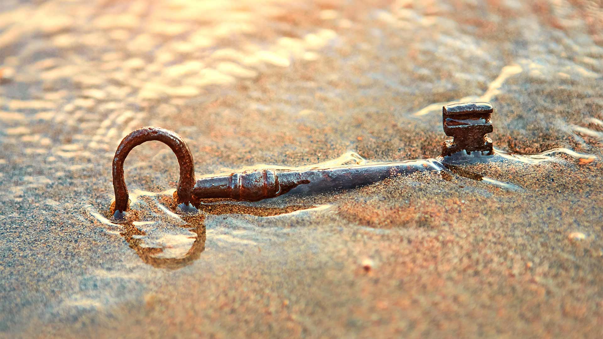 Lost key buries half in sand on a beach