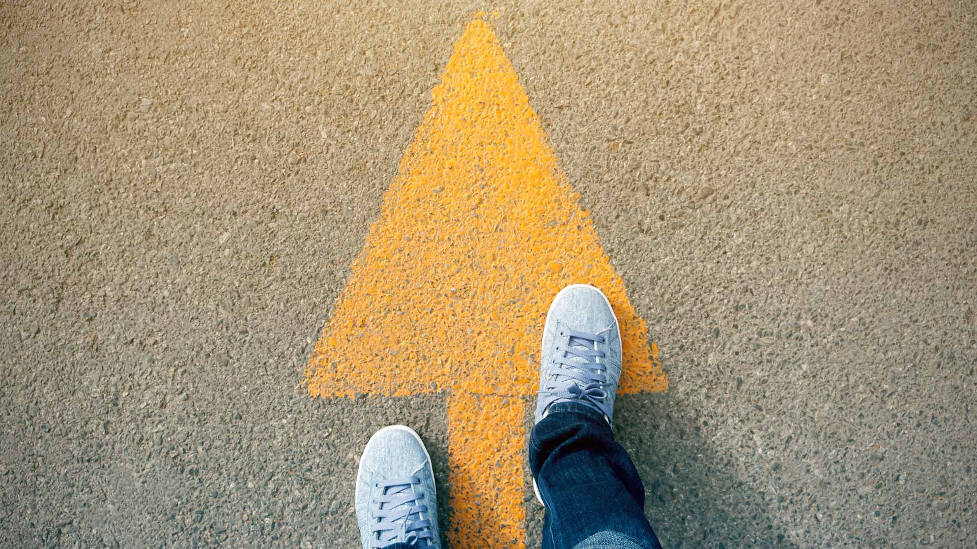Person standing on a yellow arrow painted on the ground, moving forward