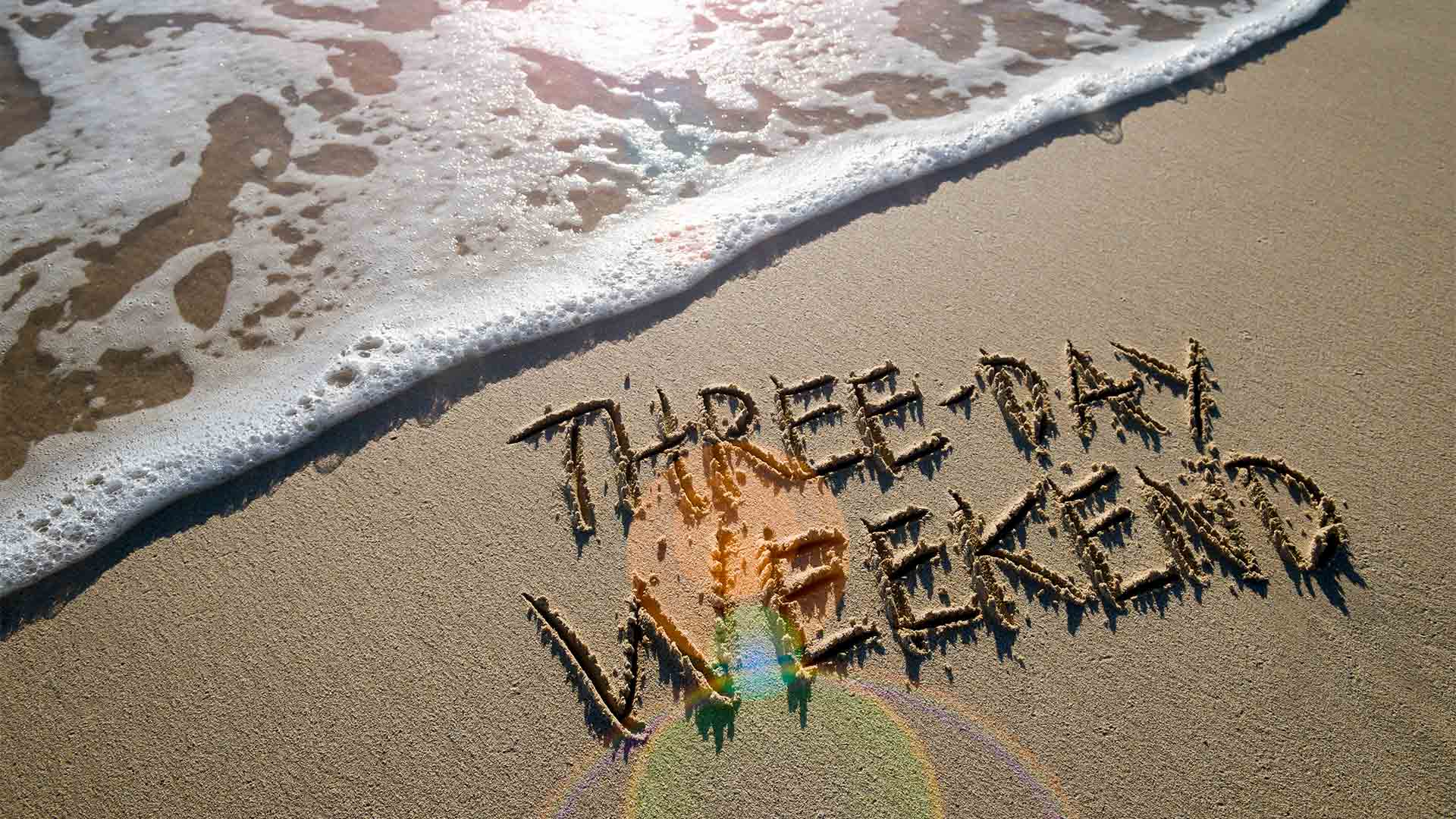 Three day weekend written in sand on a beach