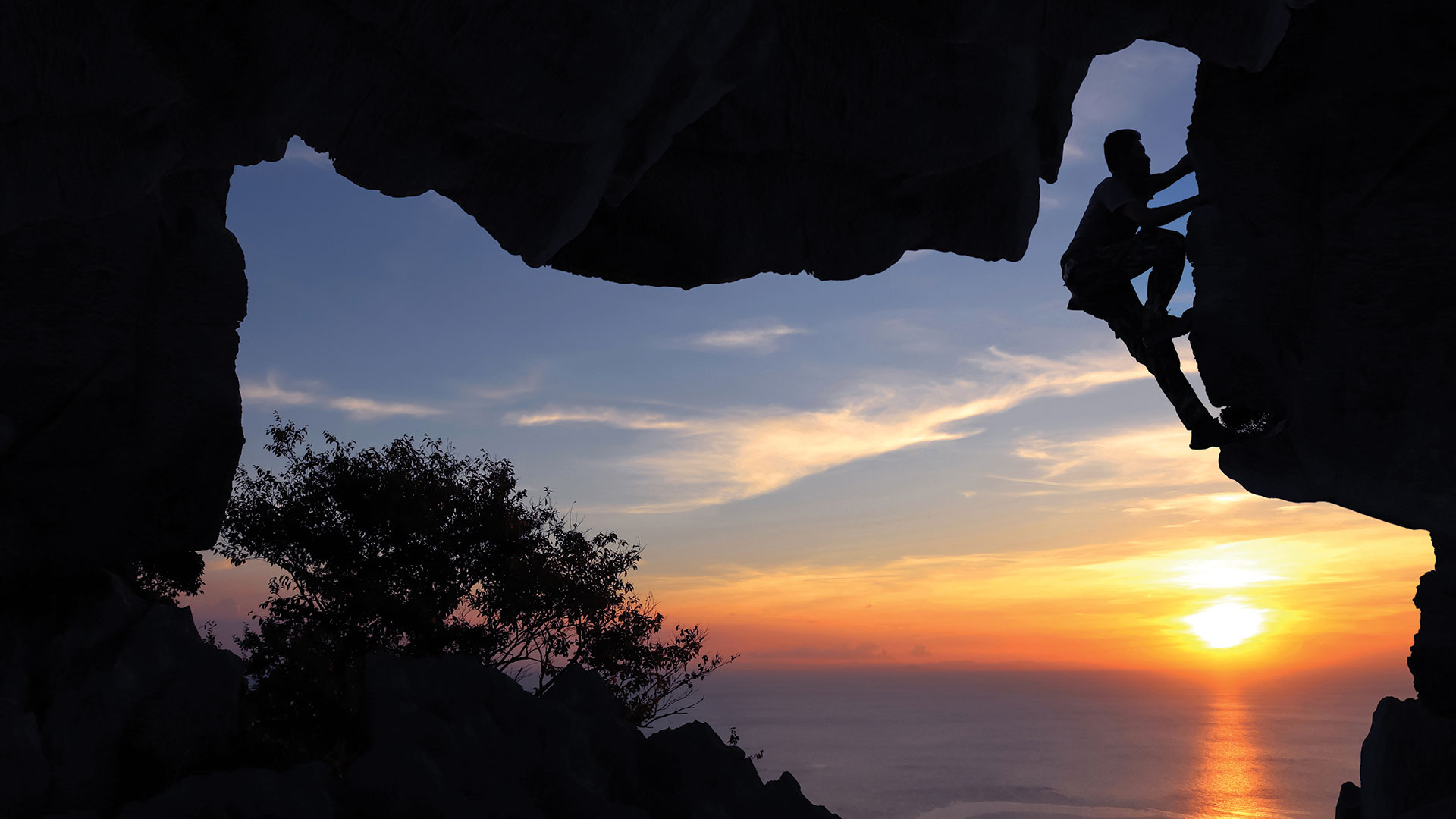Man climbing in cave on mountain at sunset