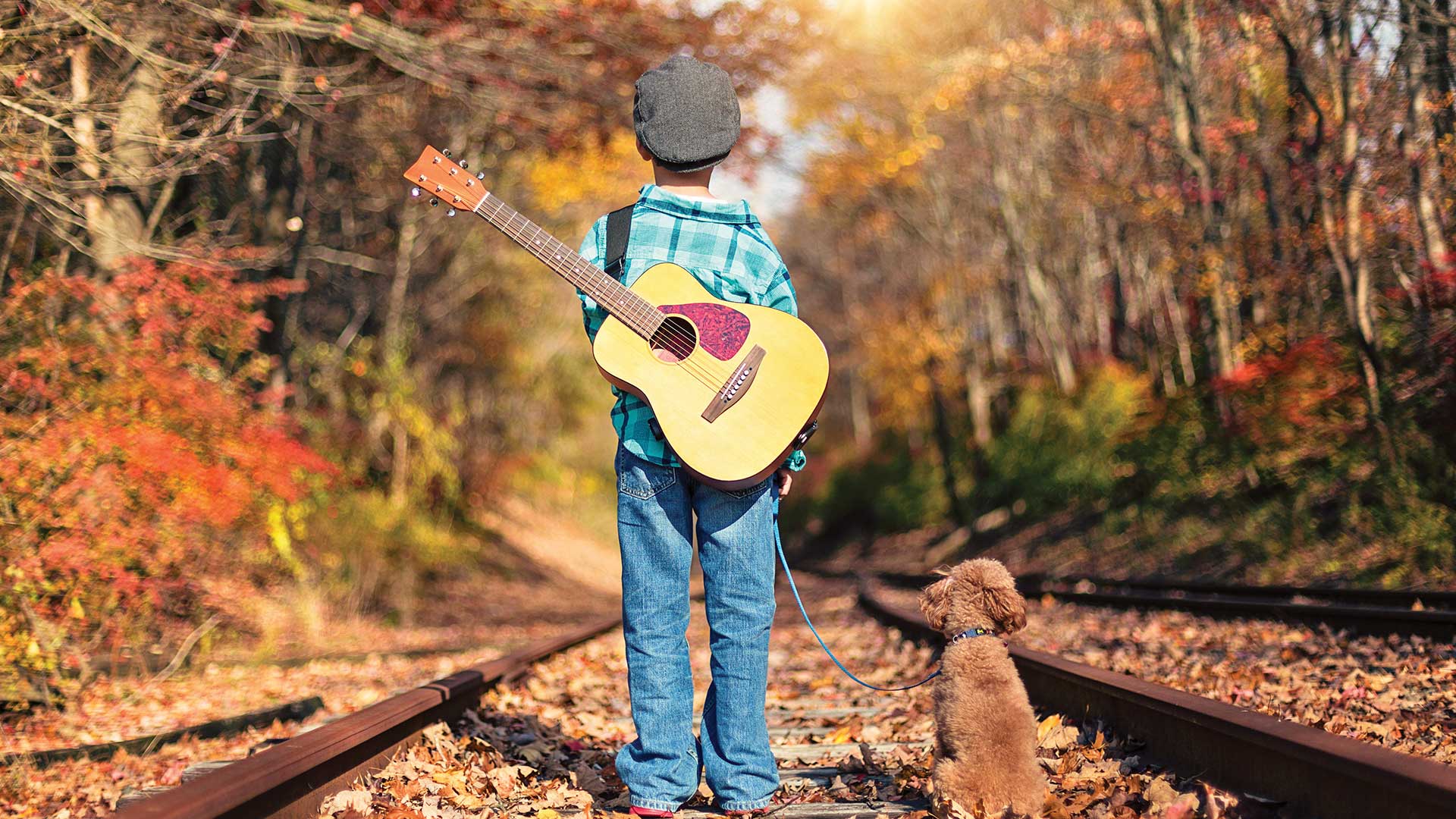 Little boy with guitar and dog walking along the railroad