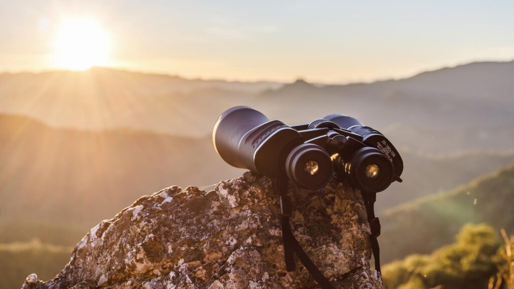 Binoculars on top of a rock looking out at the beautiful mountains at sunset