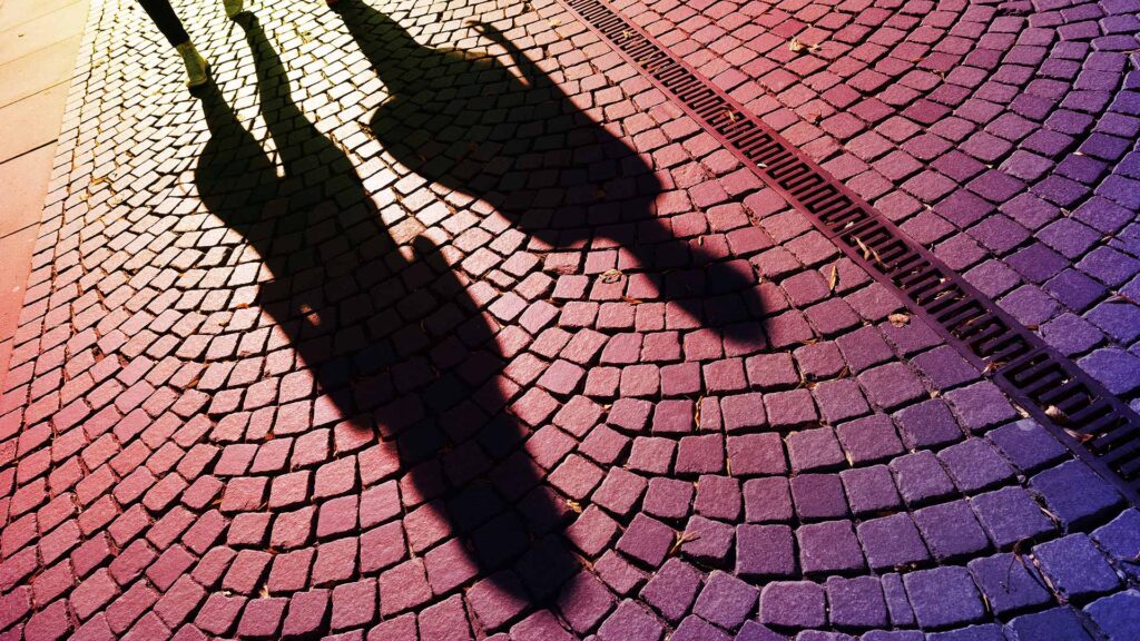 Two shadows of people walking on pavement