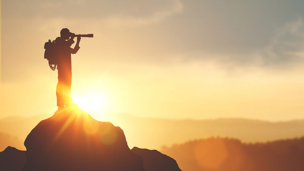 Silhouette of person looking through binoculars whilst standing on rock