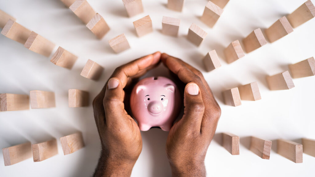 Person protecting piggy bank from falling jenga blocks with their hands