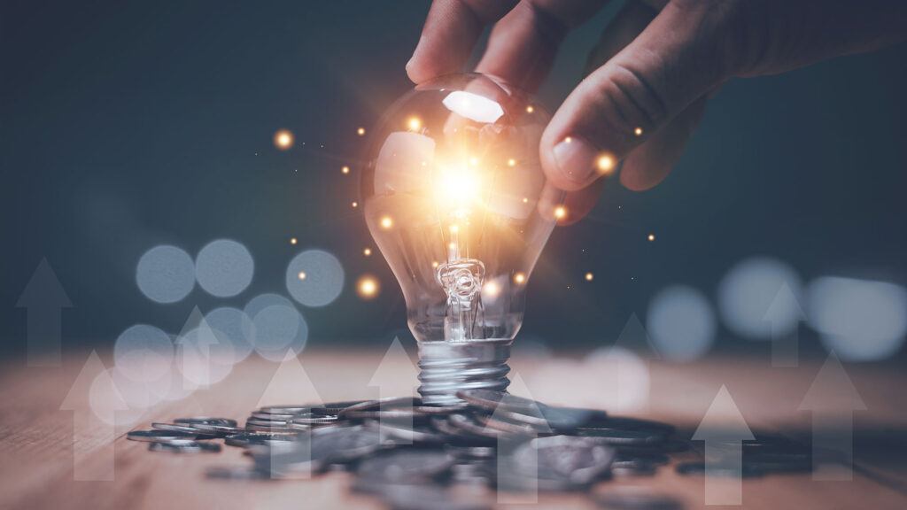 Lit up lightbulb with pile of coins below