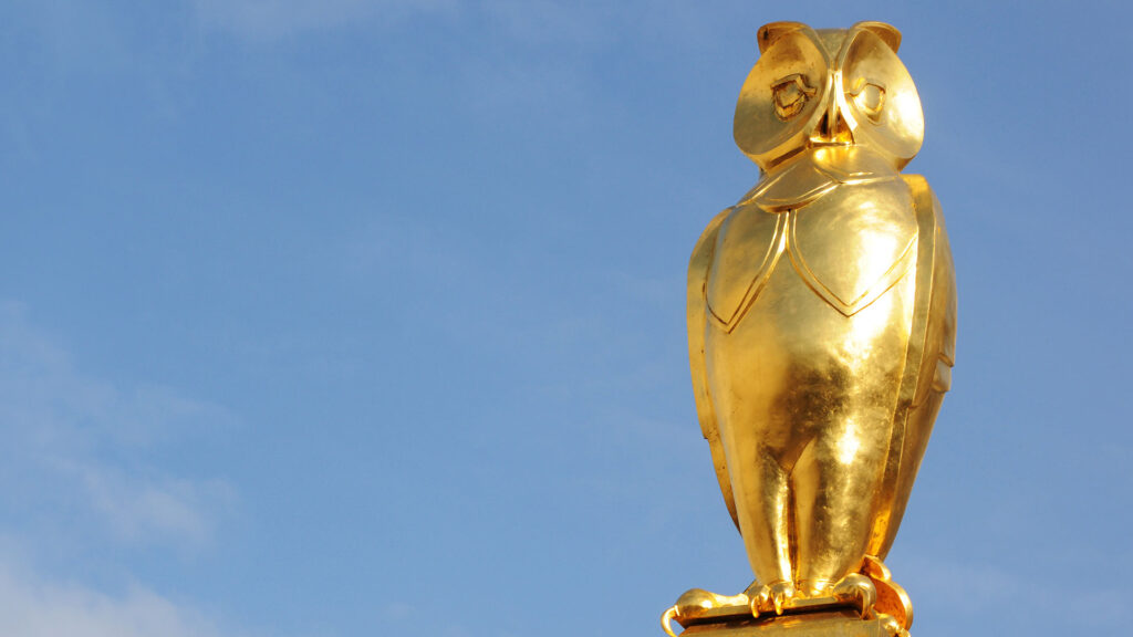 Golden owl sculpture against blue background