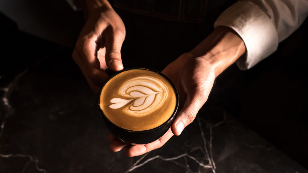 Barista holding cup of coffee with foam art on top
