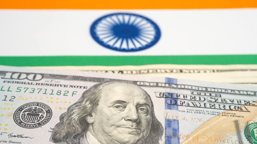 A one hundred dollar bill below a Indian flag