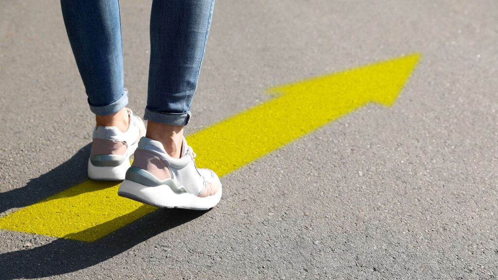 Person walking on yellow arrow on road.