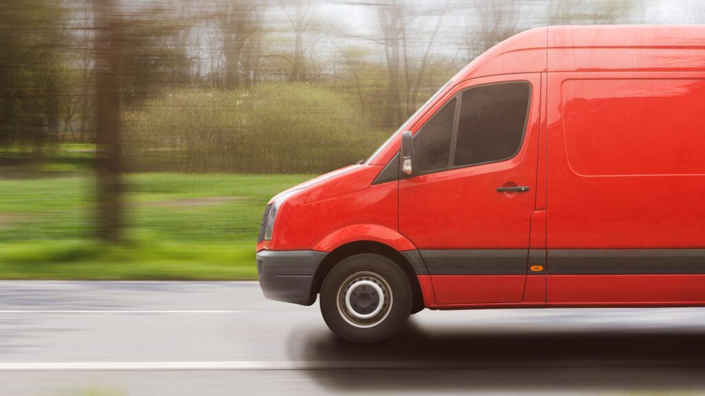 Red van driving fast with background of woods blurred