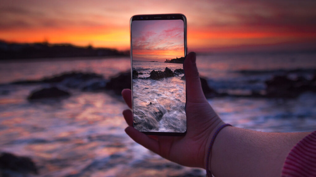 Person holding up mobile phone to take a photo of the sunset at the beach