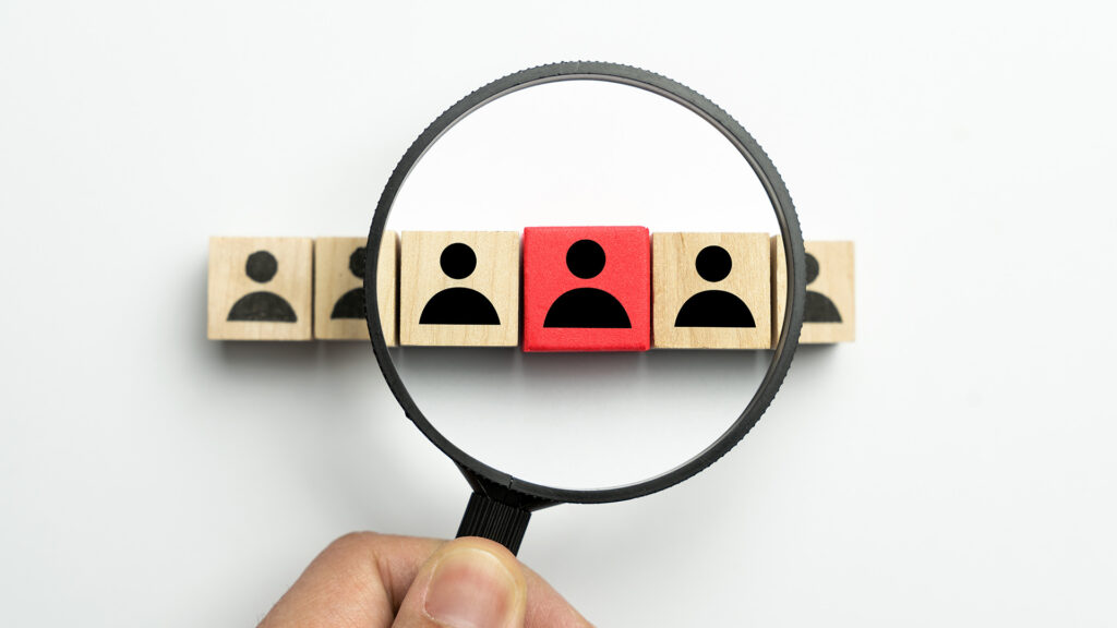 Searching for talent concept with a magnifying glass highlighting a red block out of many plain blocks