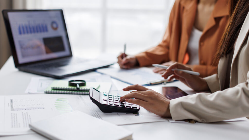 Business people using laptop and calculator whilst writing reports