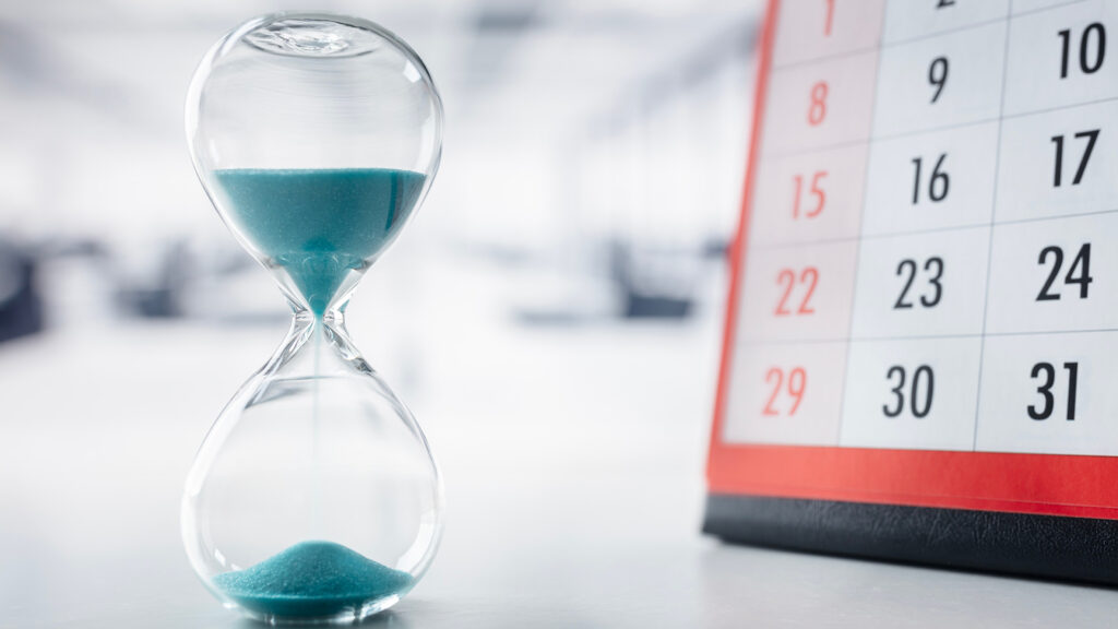 Hour glass running time with sand in front of calendar