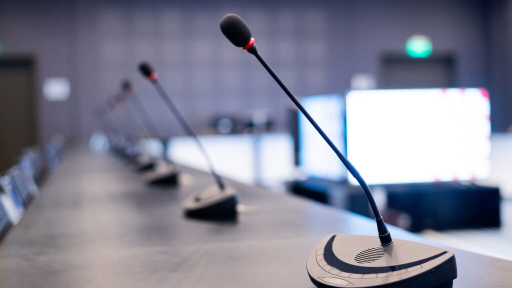 Close up of microphones on a long table, ready for debate