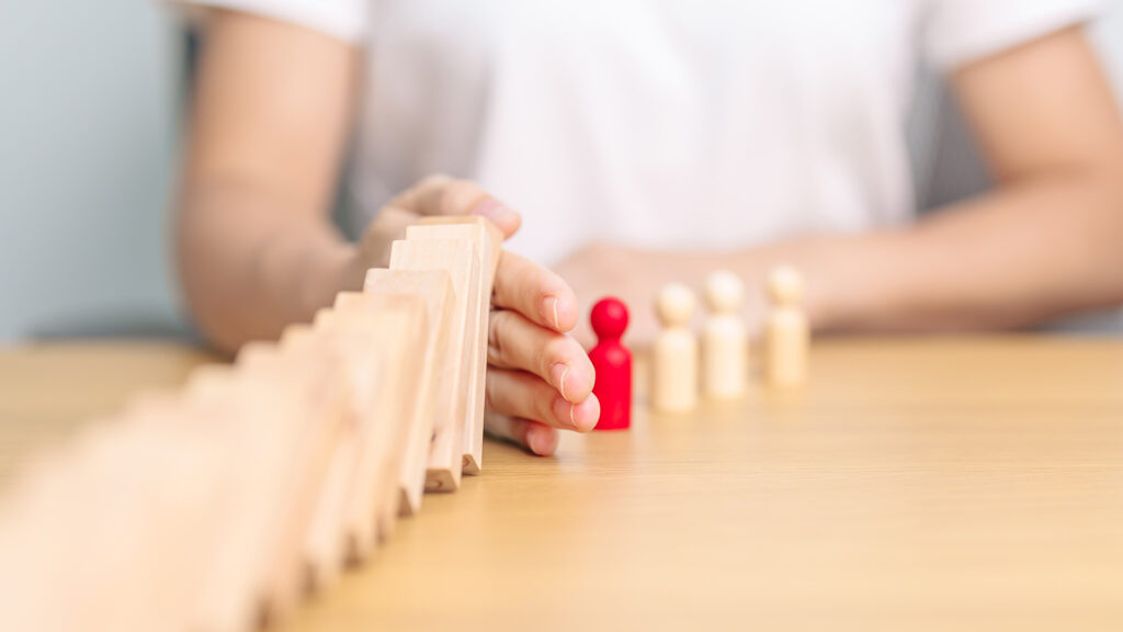 Hand stopping falling domino blocks.
